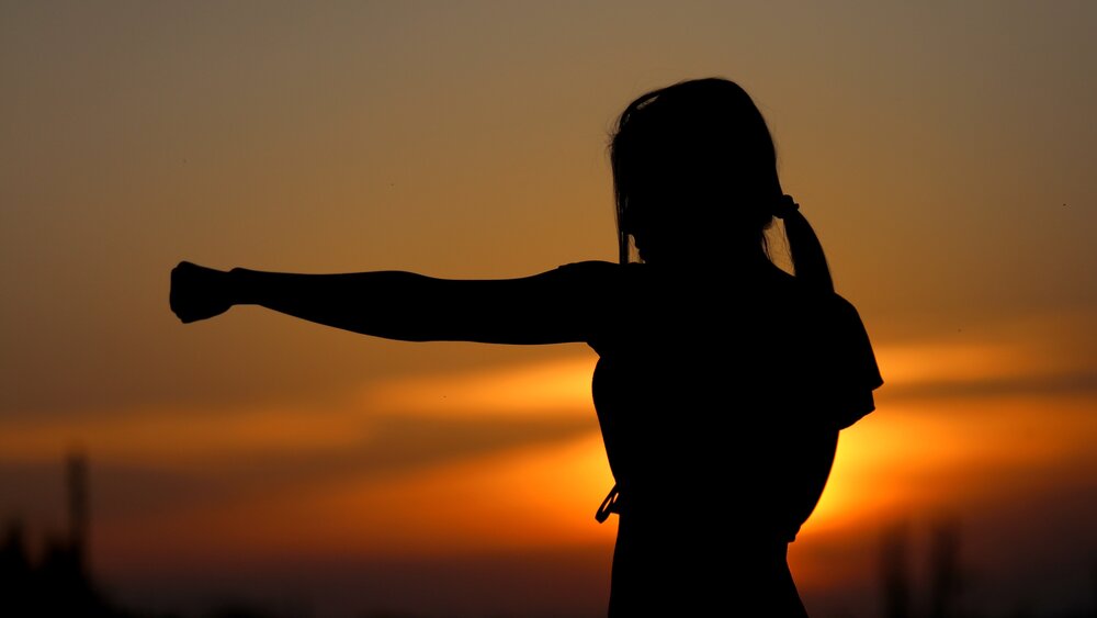 Die Silhoutte einer Frau in einer Tai Chi Pose vor einem Sonnenuntergang.